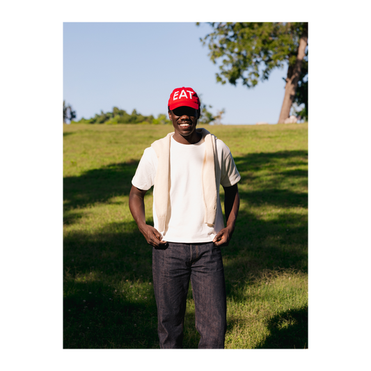 Person wearing a red cap with 'EAT' text, standing in a grassy outdoor area.