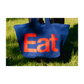 Blue tote bag with red 'Eat' text on grass