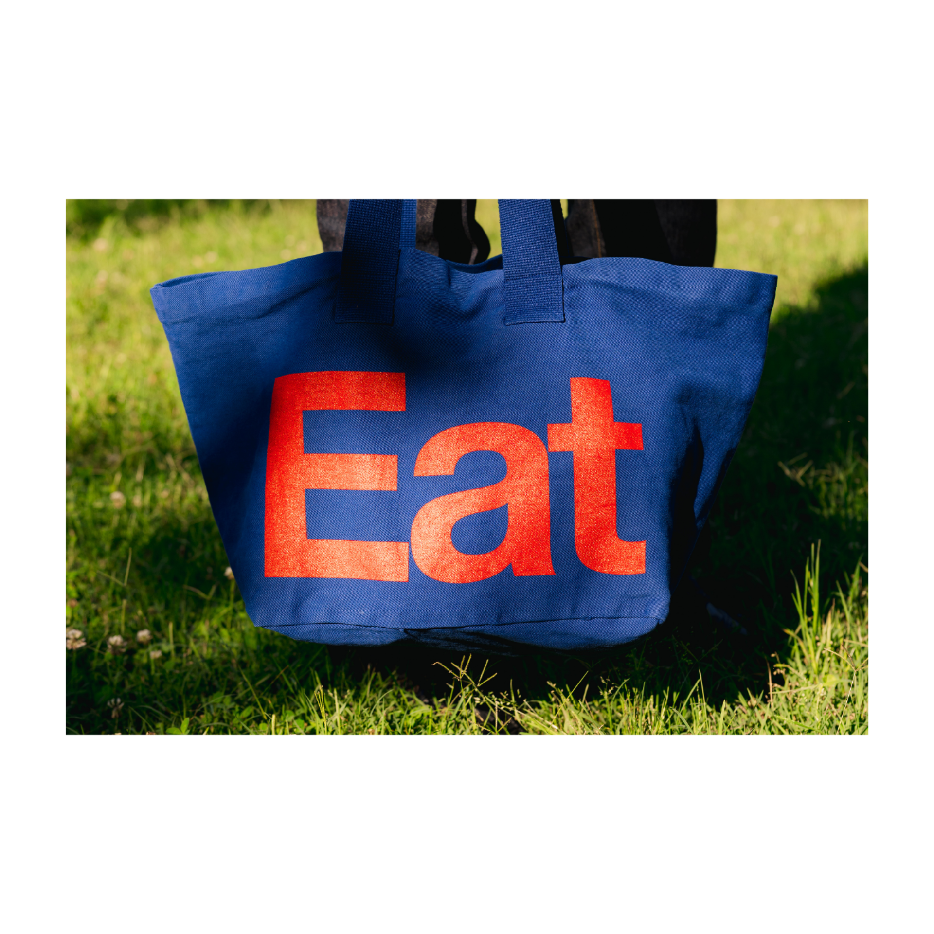 Blue tote bag with red 'Eat' text on grass