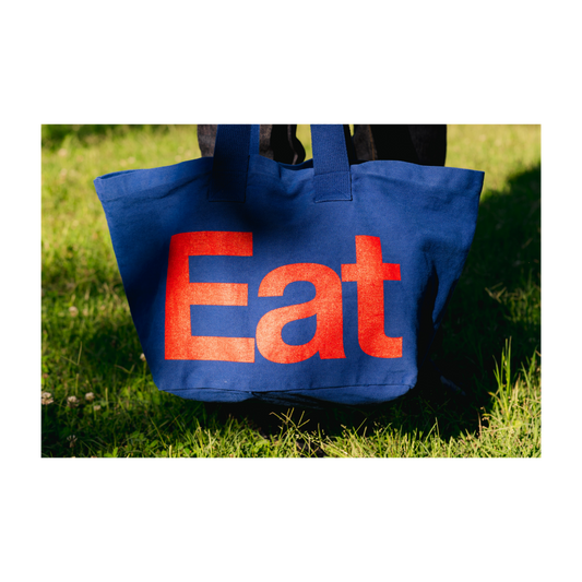Blue tote bag with red 'Eat' text on grass