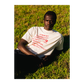 Person wearing a white t-shirt with red Eat text sitting on grass