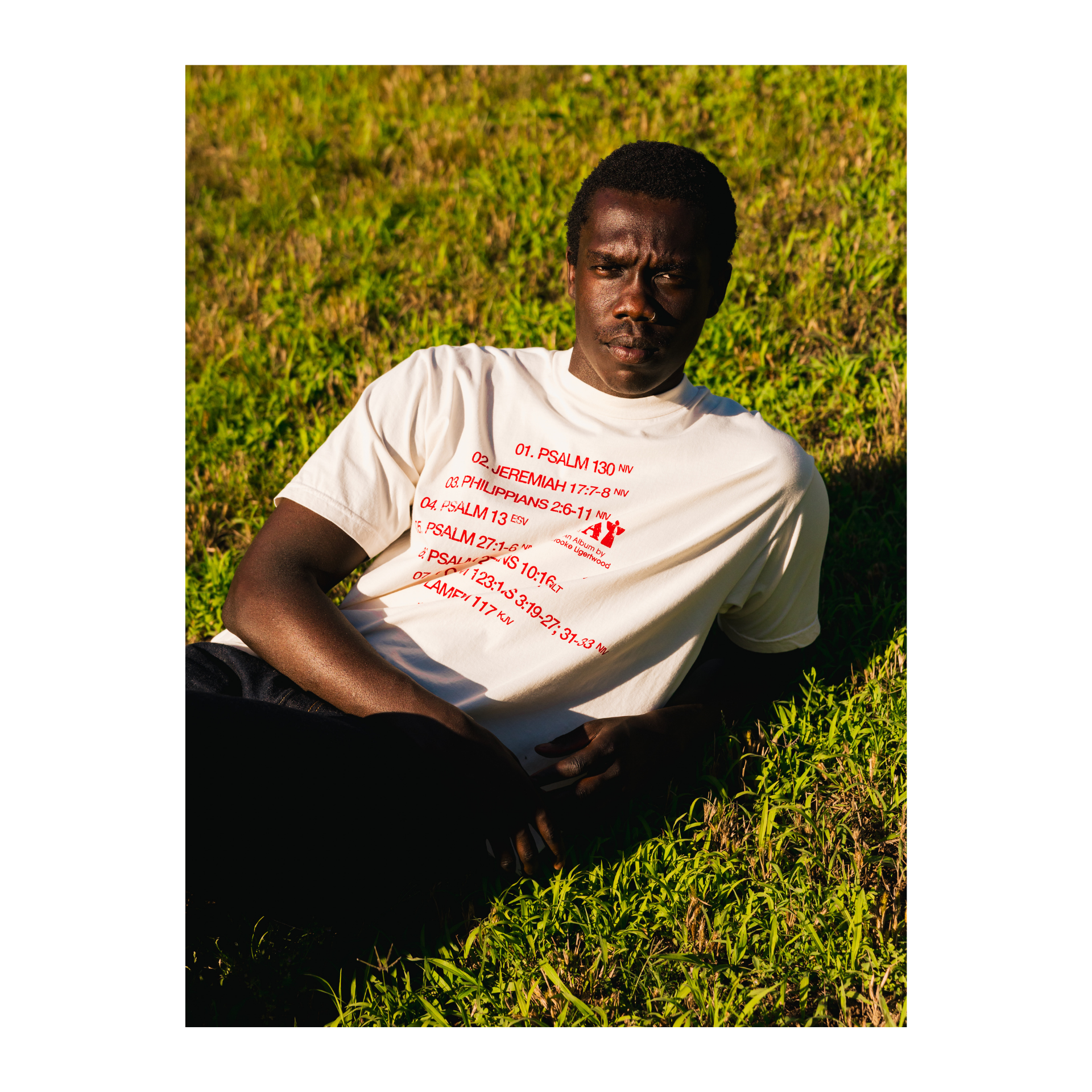 Person wearing a white t-shirt with red Eat text sitting on grass