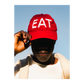 Person wearing a red cap or hat with 'EAT' text against a clear blue sky