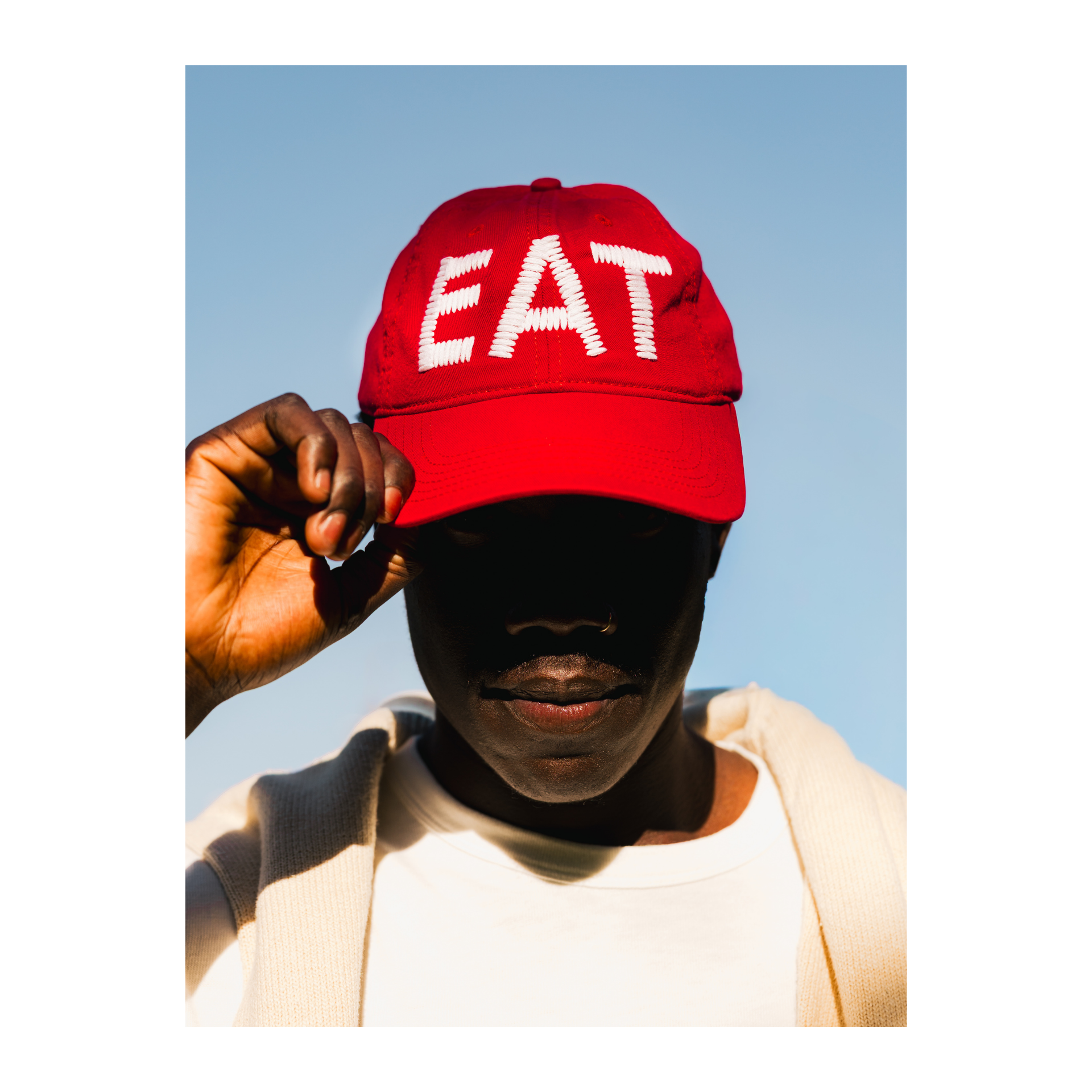 Person wearing a red cap or hat with 'EAT' text against a clear blue sky