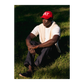 Person wearing a red cap or hat with text, sitting on grass